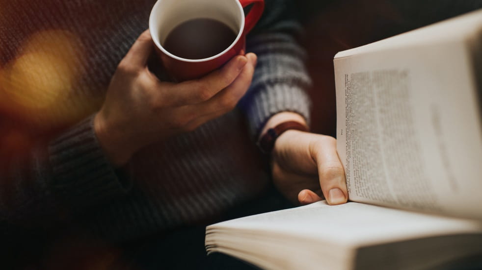 person reading a book with a warm drink